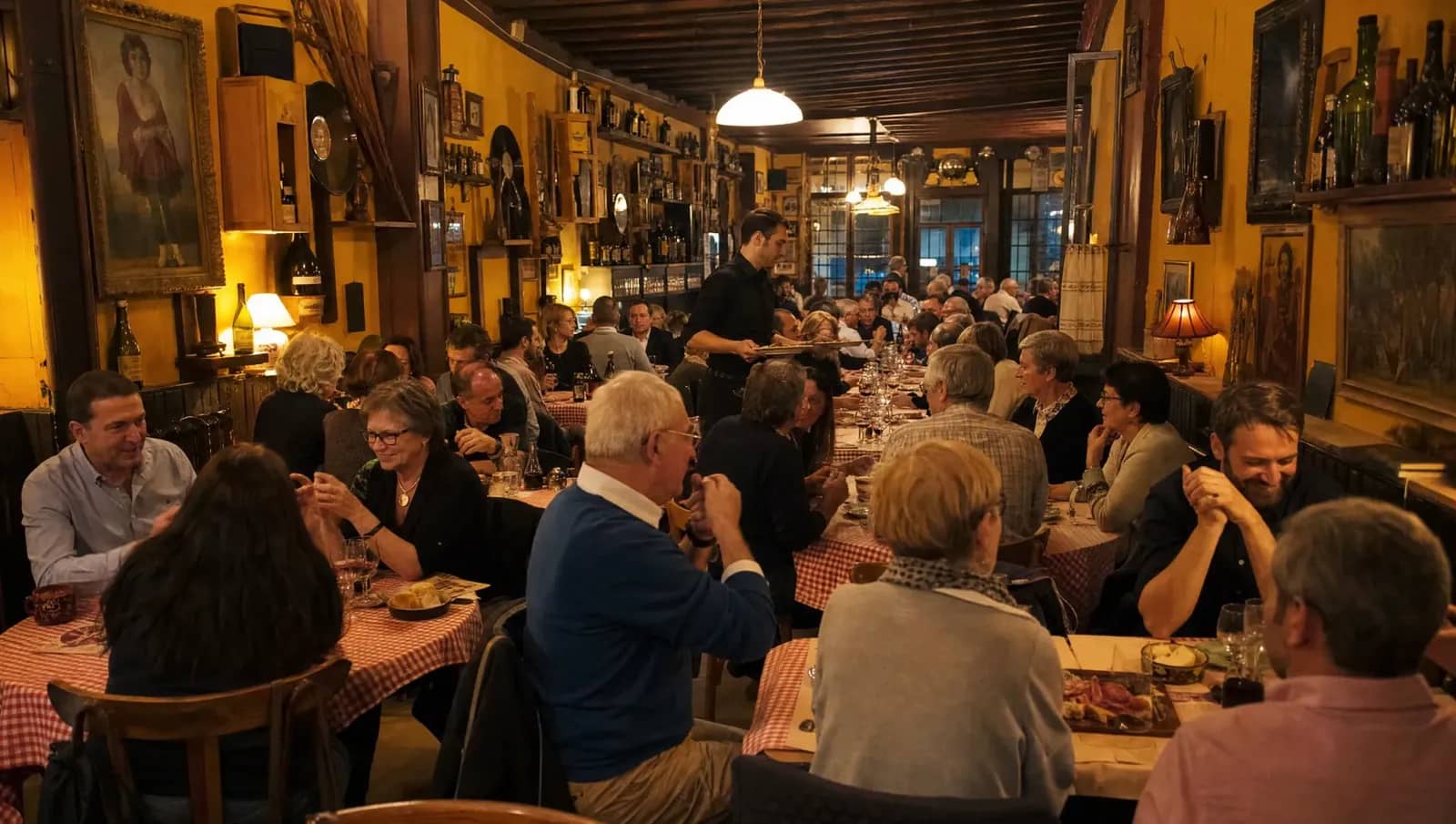 Salle d'un bouchon lyonnais pleine un soir de novembre, clients attablés autour de verres de vin rouge