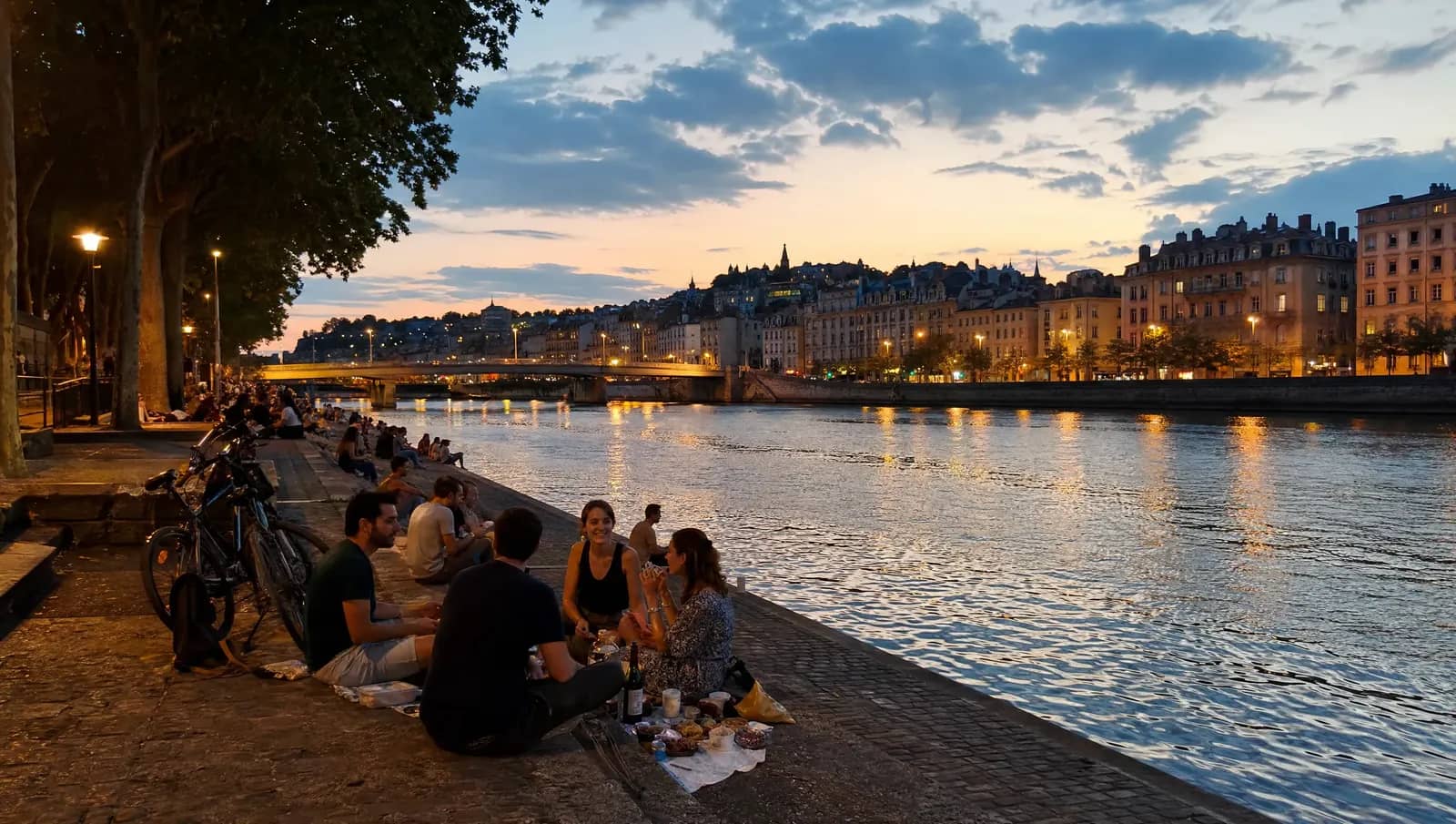 Pique-nique au crépuscule sur les bas-ports du Rhône à Lyon, vélos et groupes d'amis au bord de l'eau