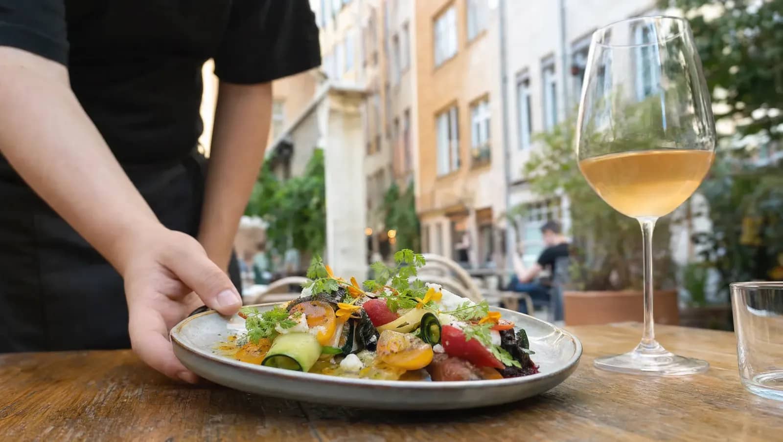 Assiette de cuisine bistronomique de saison servie en terrasse dans un restaurant lyonnais, légumes colorés et verre de vin nature