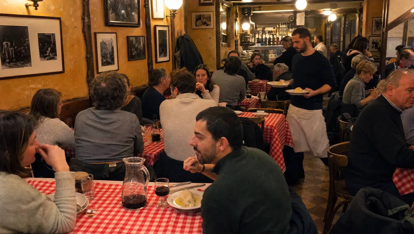 La salle comble d'un bouchon lyonnais un soir d'hiver, nappes vichy rouges et quenelle servie à table