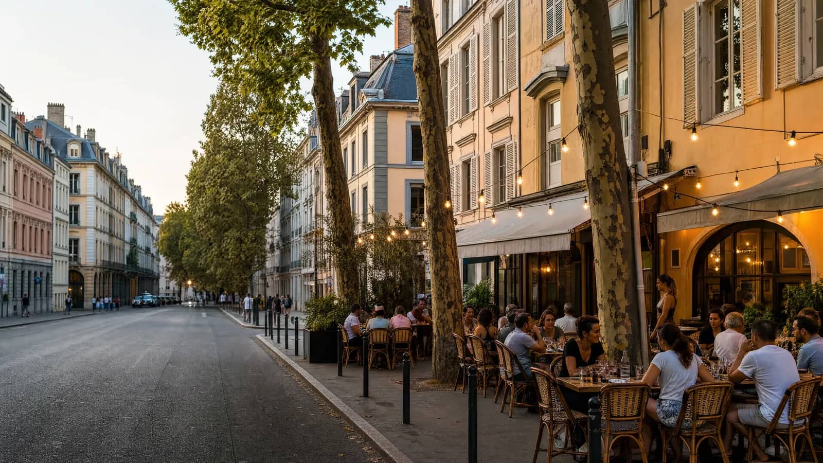 Terrasse de restaurant animée sur une rue de la Presqu'île à Lyon au coucher du soleil, façades ocre et guirlandes lumineuses