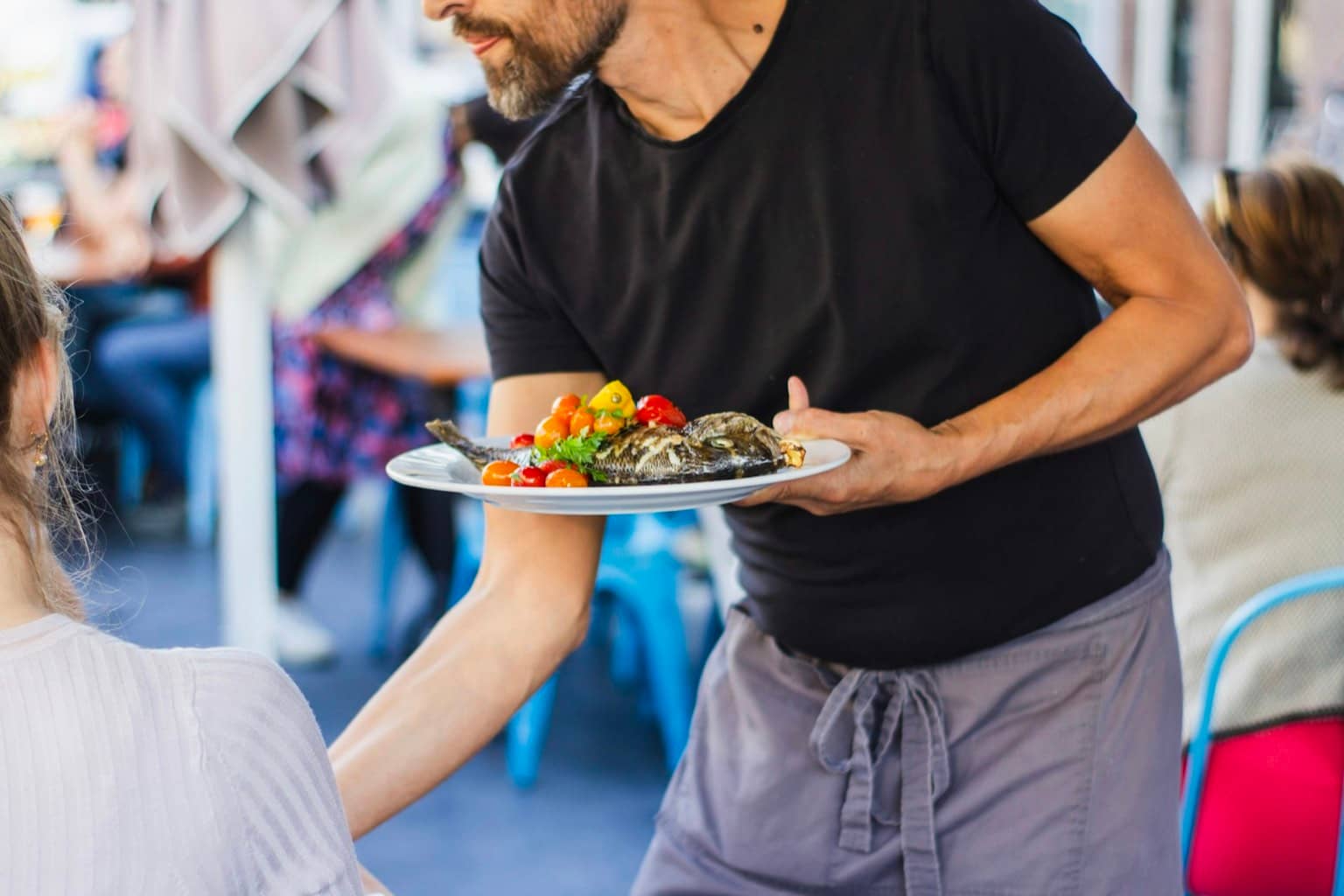 Serveur souriant servant un café à un couple en terrasse