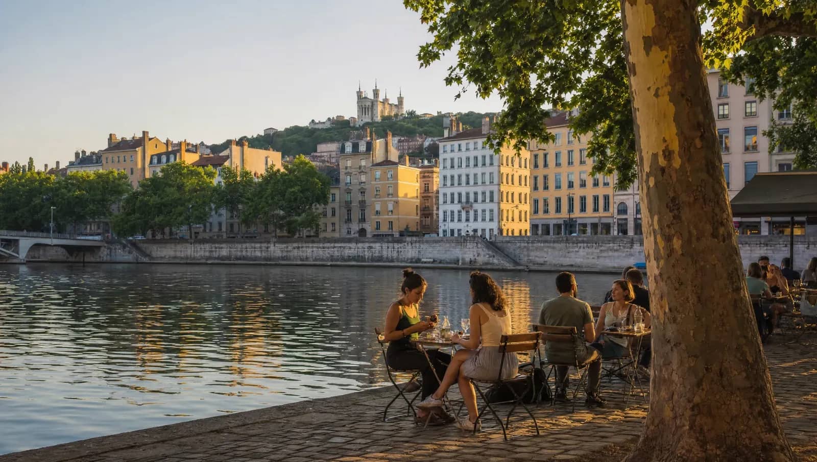 Terrasse au bord de la Saône à Lyon au coucher du soleil, avec les façades du Vieux Lyon et la basilique de Fourvière en arrière-plan