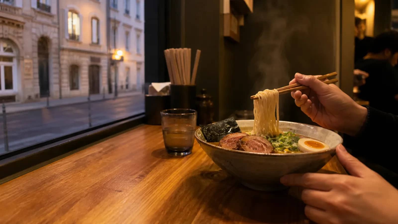 Bol de ramen fumant dégusté au comptoir face à une rue lyonnaise