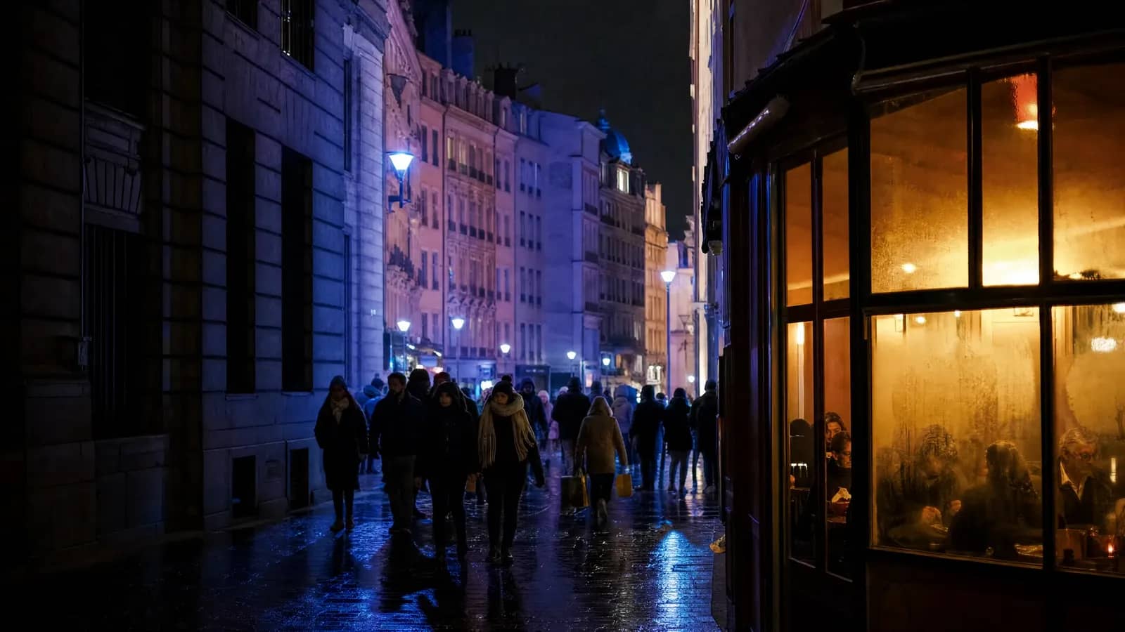 Une rue de la Presqu'île de Lyon illuminée en bleu pendant la Fête des Lumières, avec la vitrine chaleureuse d'un bistrot où des clients dînent
