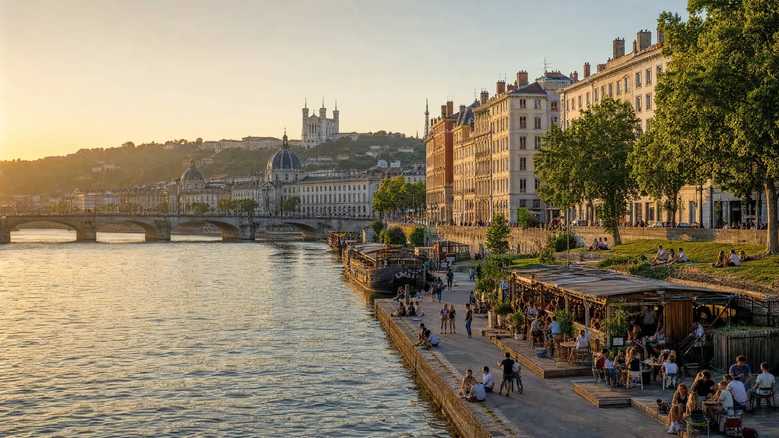 Terrasses et péniches au bord du Rhône à Lyon au coucher du soleil, avec la basilique de Fourvière en arrière-plan