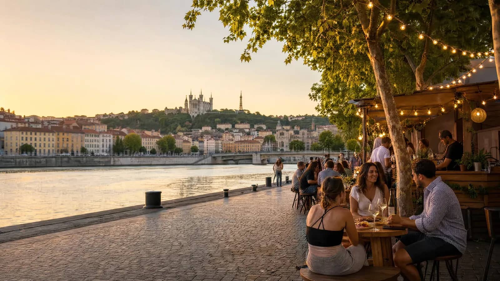 Guinguette au bord de la Saône à Lyon au coucher du soleil, tables sous les guirlandes, basilique de Fourvière en arrière-plan