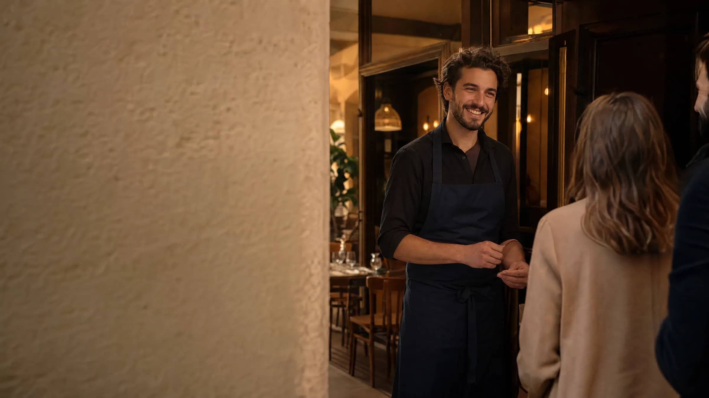 Un serveur accueille des clients à l'entrée d'un bistrot indépendant lyonnais, illustrant TheGoodSeat Pro comme alternative à Tableo qui amène de nouveaux dîneurs