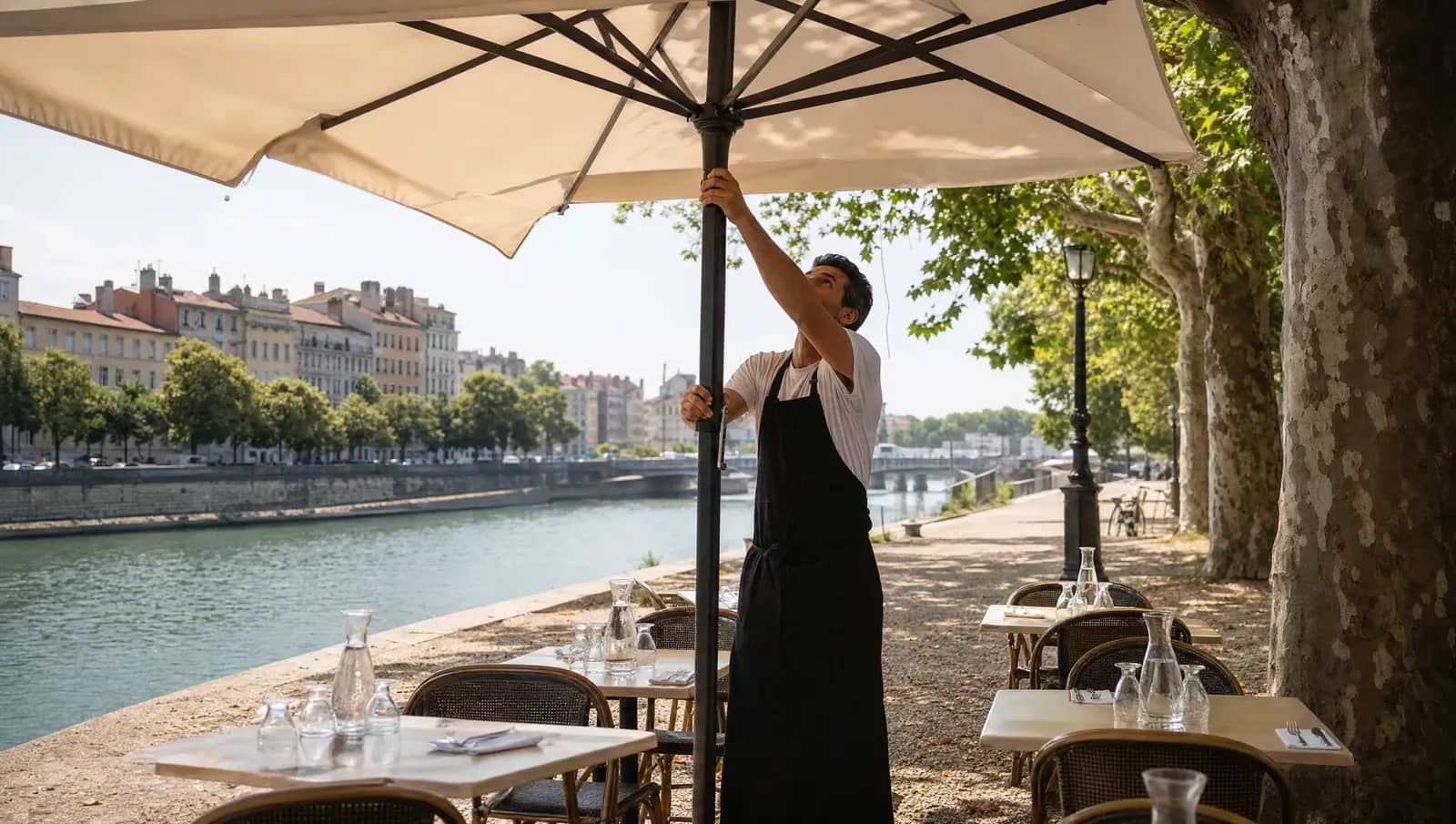 Serveur ouvrant un parasol sur une terrasse ombragée des quais à Lyon pendant la canicule