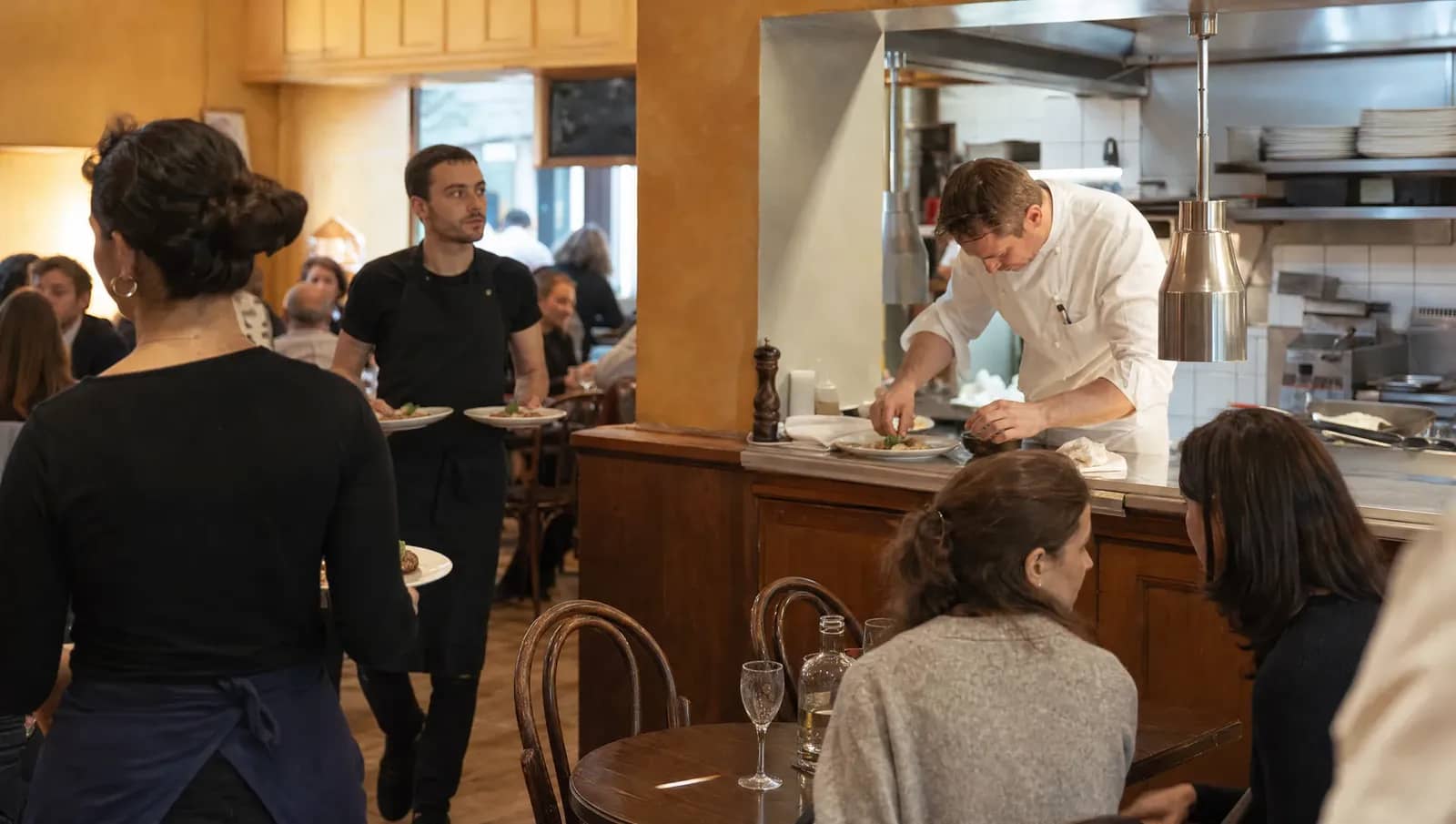 Service dans un bistrot lyonnais : un chef dresse une assiette au passe pendant que les serveurs filent en salle