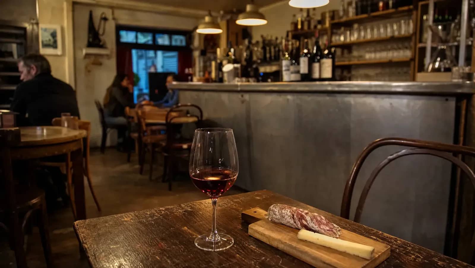 Verre de gamay et planche de saucisson sur une table en bois dans un bar à vin lyonnais, comptoir en zinc en arrière-plan