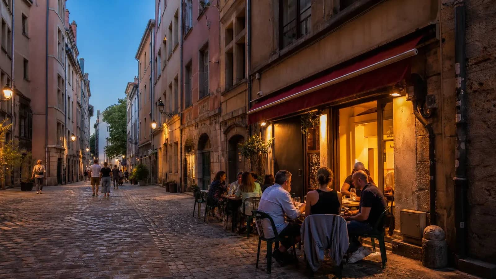 Terrasse animée dans une rue pavée du Vieux Lyon à la tombée du jour