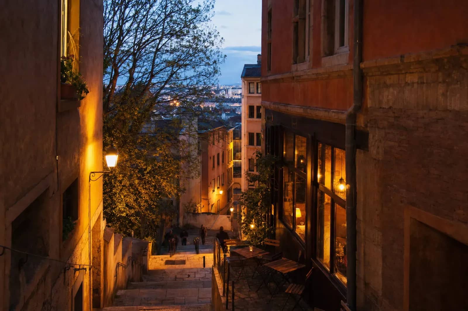 Rue en pente de la Croix-Rousse avec un bistrot aux fenêtres éclairées le soir