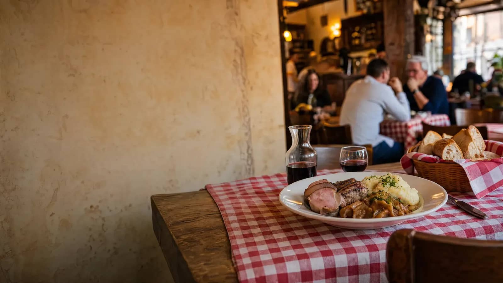 Table conviviale d'un bouchon lyonnais à la nappe vichy, assiette généreuse et carafe de vin : bien manger pas cher à Lyon.