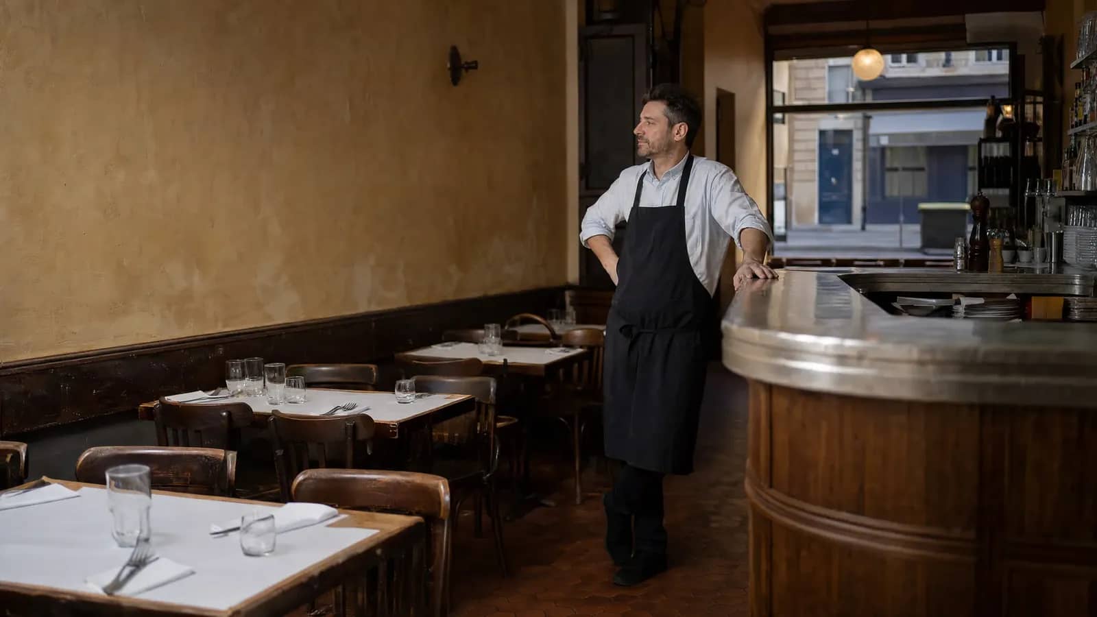 Salle d'un bouchon lyonnais presque vide un jour de basse saison, le restaurateur observe les tables dressées et désertes.