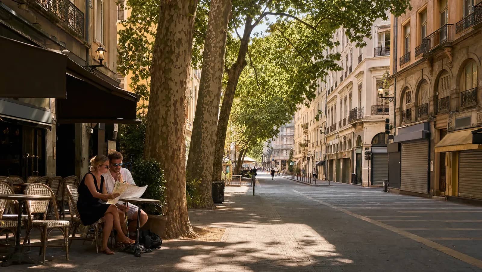 Rue de la Presqu'île à Lyon en août, boutiques aux rideaux baissés et un couple de touristes attablé à la seule terrasse ouverte.